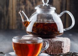 Black tea in teapot and cup with dry tea, brick side view on a wooden background