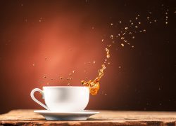 Brown splashes out drink from white cup of tea on a brown wooden background.