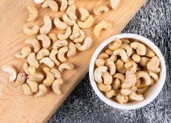 Cashew in white bowl on wooden board and black stone background